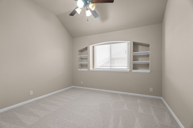 spare room with ceiling fan, light colored carpet, built in features, and vaulted ceiling