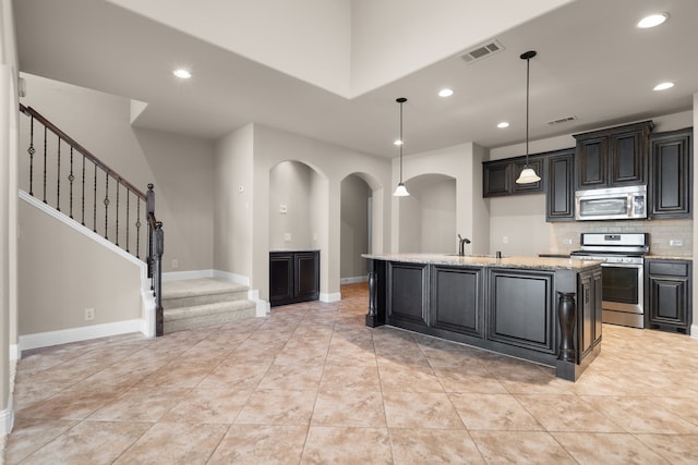 kitchen featuring light stone countertops, stainless steel appliances, tasteful backsplash, an island with sink, and pendant lighting