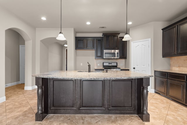 kitchen featuring light stone countertops, stainless steel appliances, sink, hanging light fixtures, and an island with sink