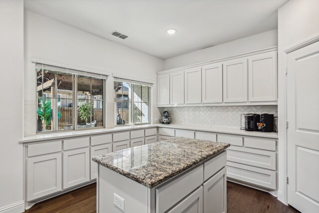 kitchen featuring light stone countertops, backsplash, white cabinets, a center island, and dark hardwood / wood-style floors