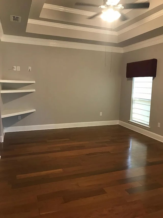 empty room with ornamental molding, a tray ceiling, ceiling fan, and dark wood-type flooring