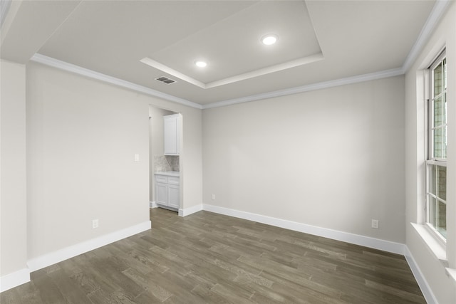 spare room featuring a raised ceiling, crown molding, and dark wood-type flooring