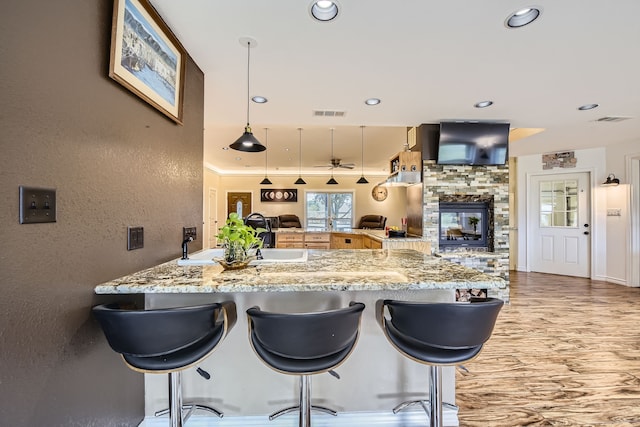 kitchen featuring a breakfast bar area, kitchen peninsula, a fireplace, and hanging light fixtures