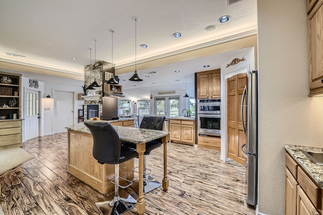 kitchen with light stone countertops, stainless steel appliances, decorative light fixtures, a center island, and light hardwood / wood-style floors