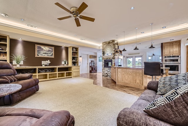 living room with a raised ceiling, ceiling fan, a fireplace, and light hardwood / wood-style flooring