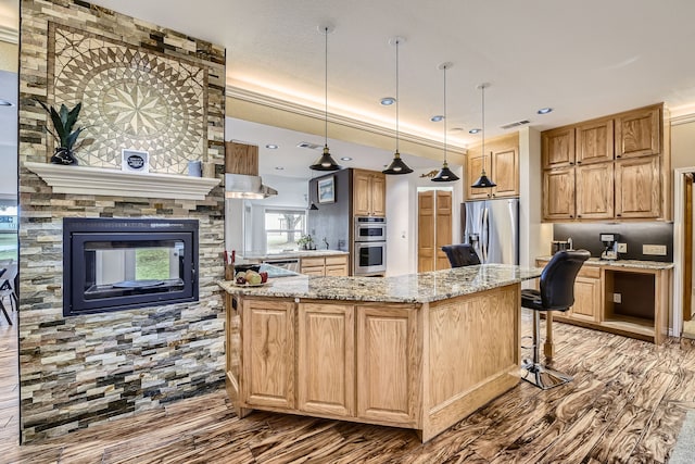 kitchen with light stone counters, stainless steel appliances, pendant lighting, hardwood / wood-style flooring, and a kitchen island