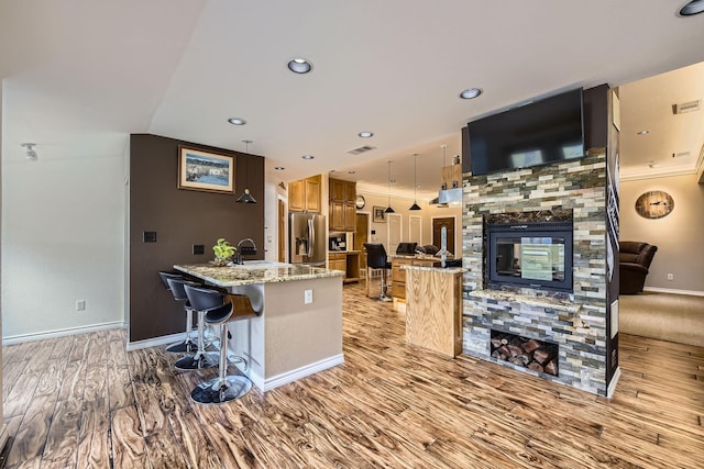 kitchen with a kitchen breakfast bar, a fireplace, stainless steel fridge with ice dispenser, light hardwood / wood-style floors, and a kitchen island