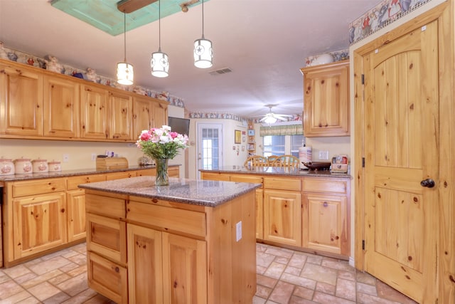 kitchen with light stone countertops, ceiling fan, light brown cabinets, a center island, and hanging light fixtures