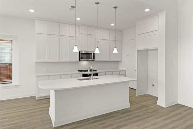 kitchen with sink, white cabinetry, hanging light fixtures, light wood-type flooring, and an island with sink