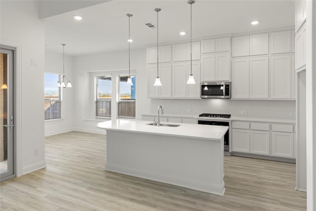 kitchen featuring sink, stove, hanging light fixtures, white cabinets, and a center island with sink