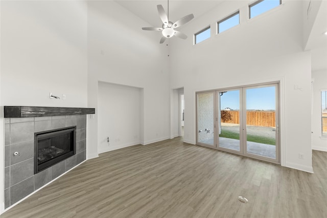 unfurnished living room featuring hardwood / wood-style flooring, ceiling fan, a tile fireplace, and a high ceiling