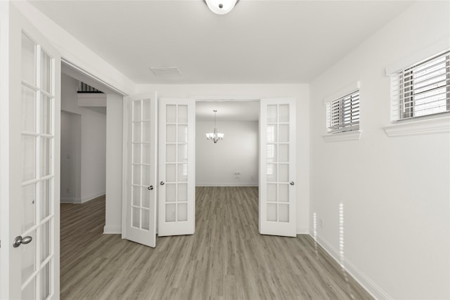 hall featuring light hardwood / wood-style flooring, a notable chandelier, and french doors