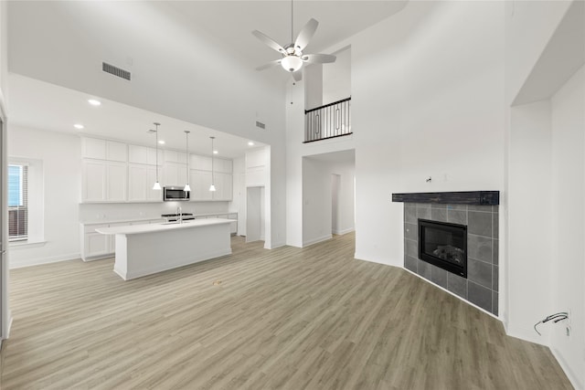 unfurnished living room with a fireplace, sink, a high ceiling, ceiling fan, and light hardwood / wood-style flooring