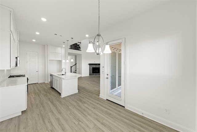 kitchen with sink, a center island with sink, white cabinets, and decorative light fixtures