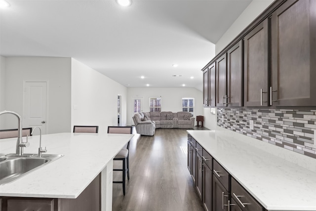 kitchen with a kitchen bar, sink, an island with sink, and dark wood-type flooring