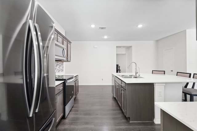 kitchen with appliances with stainless steel finishes, a kitchen breakfast bar, dark brown cabinetry, sink, and dark hardwood / wood-style floors