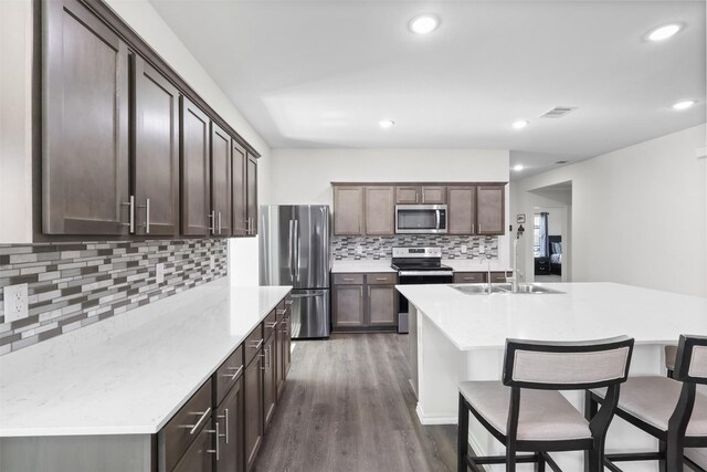 kitchen featuring sink, decorative backsplash, an island with sink, appliances with stainless steel finishes, and dark hardwood / wood-style flooring