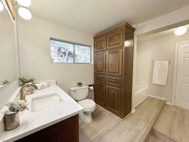 full bathroom featuring hardwood / wood-style flooring, vanity, toilet, and a textured ceiling