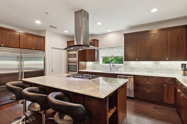 kitchen featuring island exhaust hood, light stone countertops, dark hardwood / wood-style flooring, built in appliances, and a center island