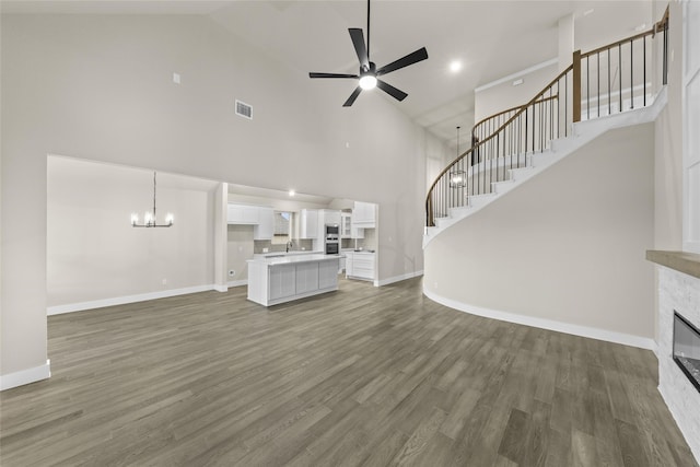 unfurnished living room with a fireplace, high vaulted ceiling, dark wood-type flooring, and ceiling fan with notable chandelier