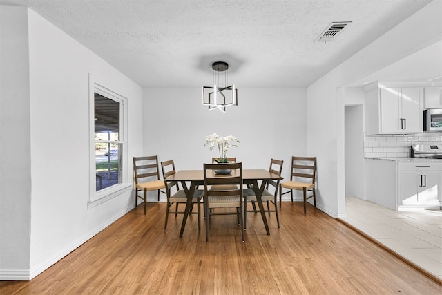 dining space featuring light wood-type flooring, a textured ceiling, and an inviting chandelier