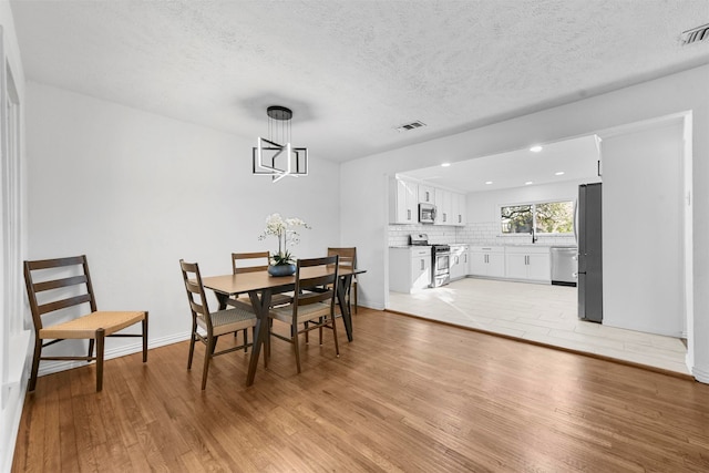 dining space with an inviting chandelier, a textured ceiling, and light wood-type flooring