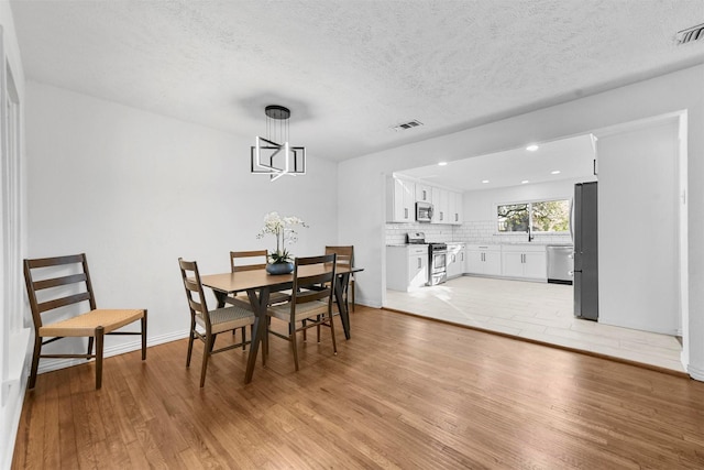 4536 Hodgkins Rd, Lake Worth, TX 76135 - dining area with light wood-style flooring, a chandelier, a textured ceiling, recessed lighting, and baseboards