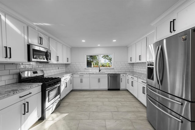 kitchen featuring appliances with stainless steel finishes, backsplash, light stone counters, sink, and white cabinets