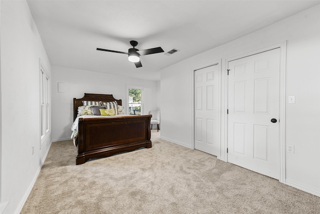 bedroom with light carpet, two closets, and ceiling fan