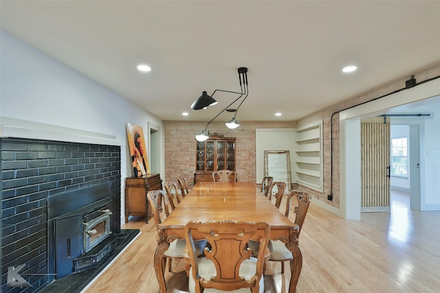 dining space with a wood stove, brick wall, and light wood-type flooring