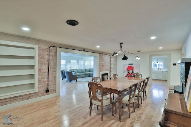 dining space with built in shelves, light hardwood / wood-style floors, and a brick fireplace