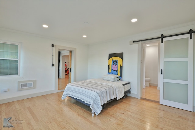 bedroom featuring a barn door, light wood-type flooring, crown molding, and connected bathroom