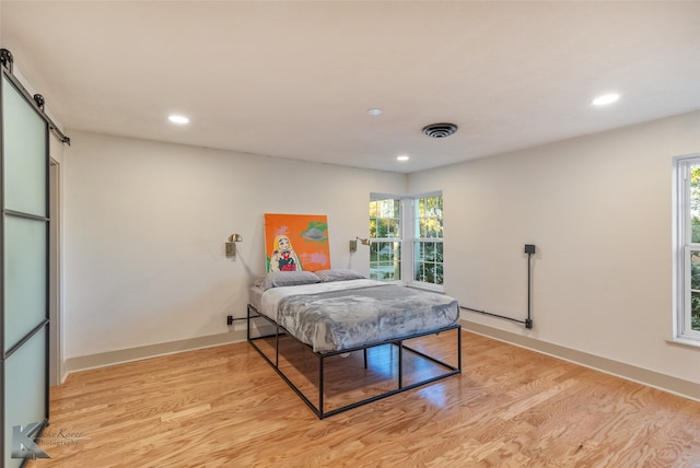 bedroom featuring a barn door, light hardwood / wood-style flooring, and multiple windows