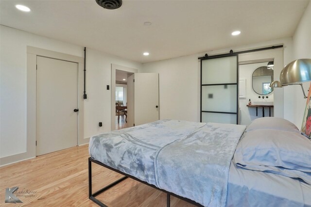 bedroom featuring a barn door, ensuite bath, and light wood-type flooring