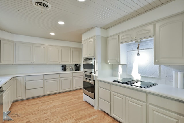 kitchen featuring black electric stovetop, light wood-type flooring, tasteful backsplash, stainless steel double oven, and white cabinetry