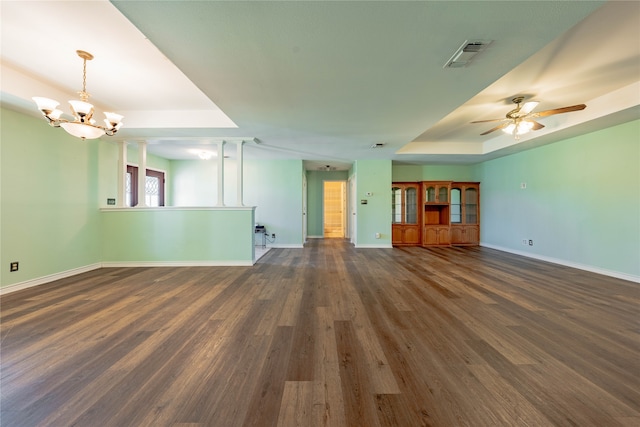 unfurnished living room with ceiling fan with notable chandelier, a tray ceiling, and dark wood-type flooring