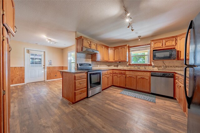 kitchen featuring hardwood / wood-style floors, appliances with stainless steel finishes, a textured ceiling, and wood walls