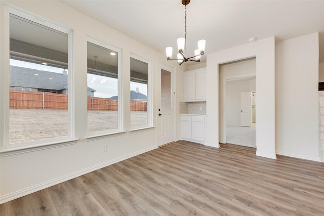 unfurnished dining area with light wood-type flooring, baseboards, and a chandelier