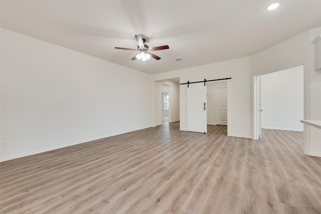 unfurnished bedroom featuring a walk in closet, a barn door, a ceiling fan, light wood-type flooring, and baseboards