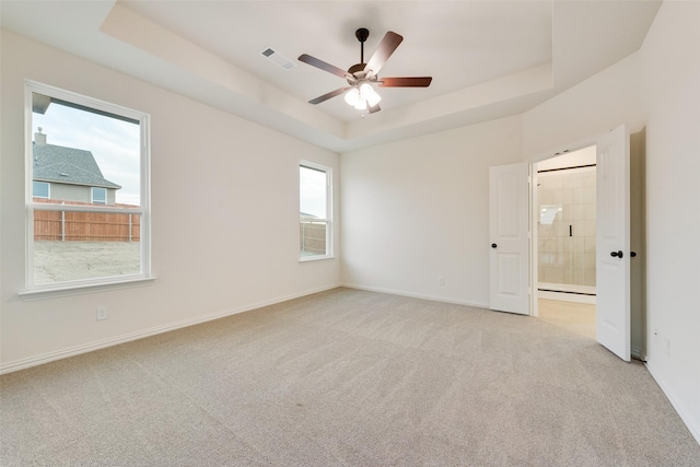 empty room featuring a tray ceiling, visible vents, a ceiling fan, light carpet, and baseboards