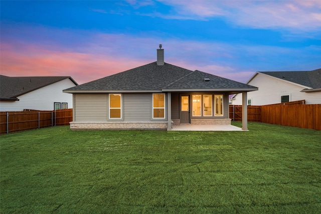 back of property at dusk featuring a yard, a patio, a chimney, a shingled roof, and a fenced backyard