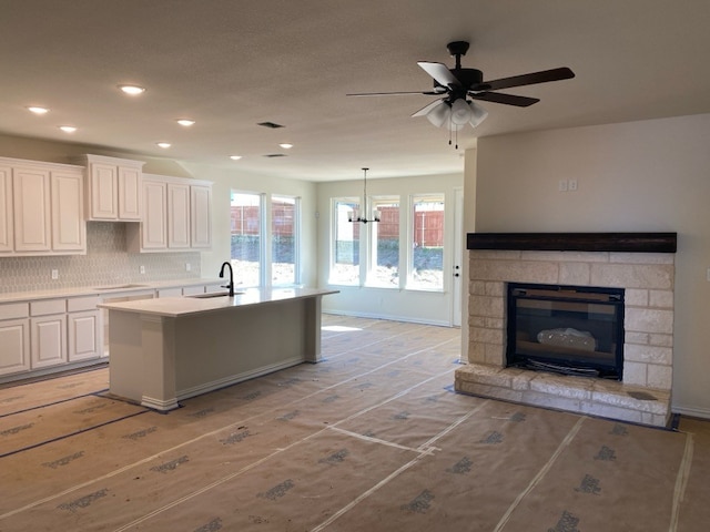 kitchen featuring an island with sink, tasteful backsplash, decorative light fixtures, cooktop, and white cabinetry