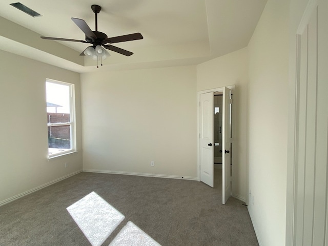 empty room with dark colored carpet, ceiling fan, and a tray ceiling