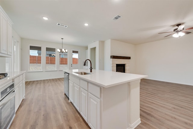 kitchen with a stone fireplace, oven, a sink, visible vents, and light wood-type flooring