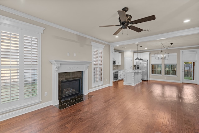 unfurnished living room with ceiling fan with notable chandelier, dark hardwood / wood-style flooring, crown molding, and a tiled fireplace