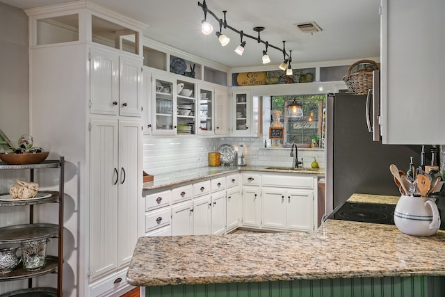 kitchen featuring sink, light stone counters, kitchen peninsula, decorative backsplash, and white cabinets