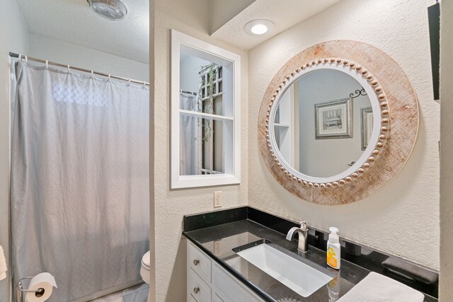 bathroom featuring a textured ceiling, vanity, toilet, and walk in shower