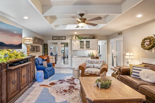 tiled living room with ceiling fan, a tray ceiling, and french doors