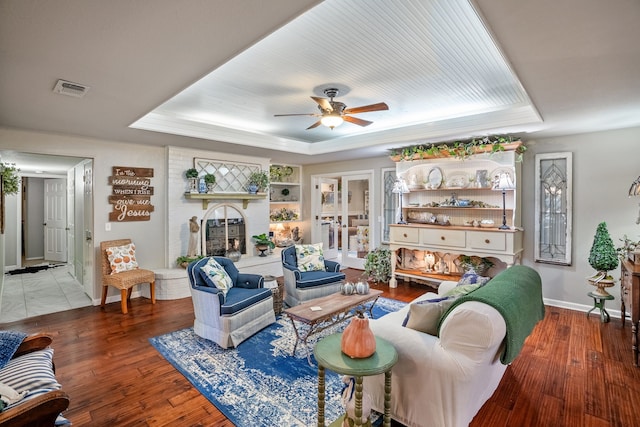 living room featuring ceiling fan, a raised ceiling, wood-type flooring, and a fireplace