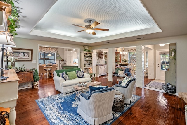 living room featuring wood-type flooring, decorative columns, a raised ceiling, and ceiling fan